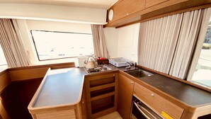 A compact kitchen with a stove, sink, and oven, wooden cabinetry, and a window with curtains. - Sun-Kissed Sailing Adventure in the Ionian Islands, Lefkada (Lefkada)