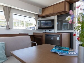 A compact RV kitchen with a microwave, refrigerator, and dining area. - Sun-Kissed Sailing Adventure in Sibenik, Croatia (Primošten)
