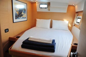 Ein ordentlich bezogenes Bett mit Kissen, ein kleines Fenster mit Vorhängen und ein gerahmtes Bild an der Wand.