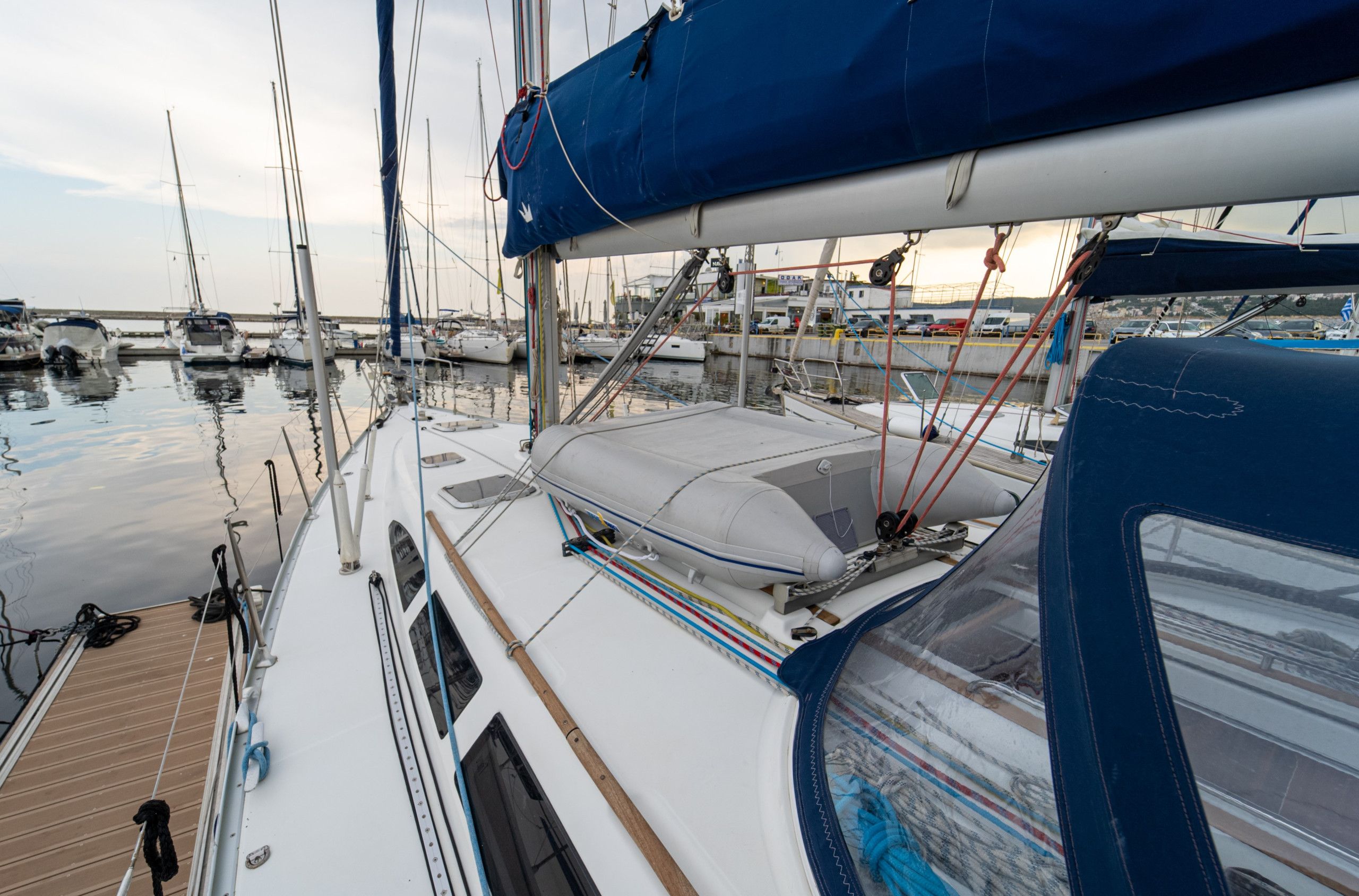 Een zeilboot afgemeerd in een jachthaven, met diverse boten, een overdekt dek en een uitzicht op de jachthaven op de achtergrond.