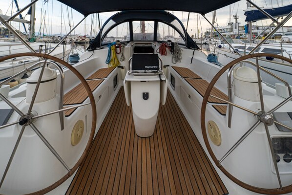 A boat deck with a central steering wheel, a Raymarine navigation system, and a wooden floor.