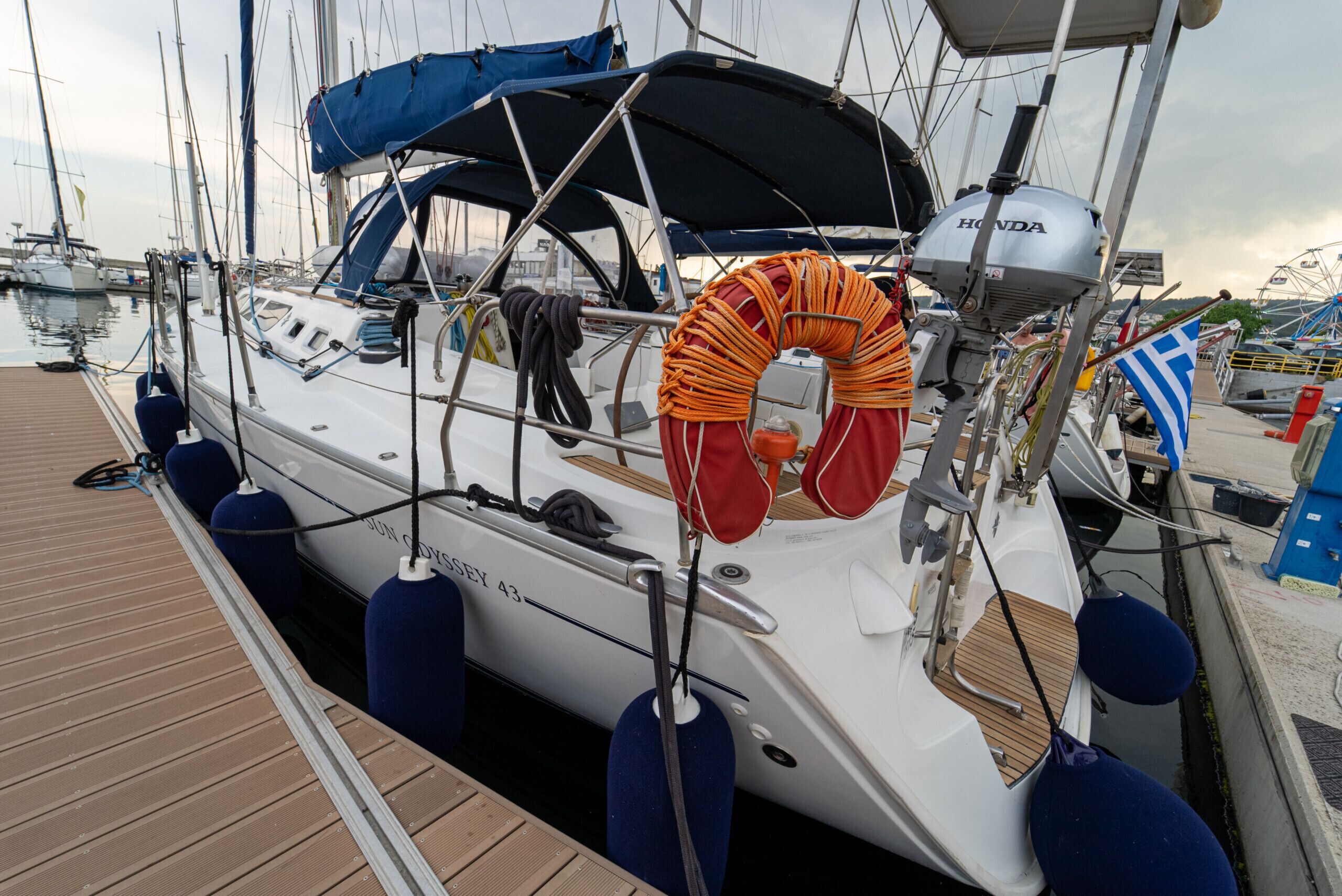 Un velero amarrado en un puerto deportivo con una cabina cubierta, un flotador salvavidas y el nombre 'SUN COYSEY 43' en el costado.