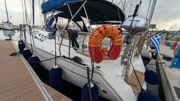 Un velero amarrado en un puerto deportivo con una cabina cubierta, un flotador salvavidas y el nombre 'SUN COYSEY 43' en el costado.