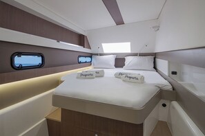 Ein kompaktes, helles Blockhaus mit einem Einzelbett, zwei Fenstern und einer kleinen Sitzecke.