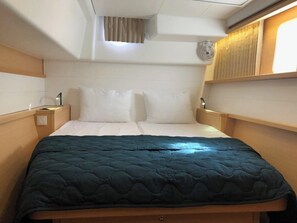 A compact bed with a dark quilt, a bedside table with a lamp, and a window with curtains. - Sun-Kissed Sailing Adventure in the Ionian Islands, Lefkada (Lefkada)