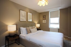 A bedroom with a bed, two bedside tables, a window with blinds, and wall art. - The Westbourne Side Story (London)