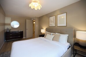 A bedroom with a large bed, a dresser, a round mirror, two framed artworks, and a ceiling light fixture. - The Westbourne Side Story (London)