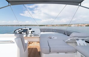 A boat deck with a steering wheel, control panel, cushioned seating, and a view of a coastal town. - Dubrovnik Delight: A Sun-Kissed Sailing Experience (Komolac)