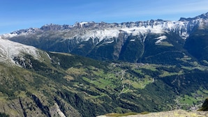 Een bergachtig landschap met besneeuwde toppen en een vallei met groene velden en verspreide gebouwen.