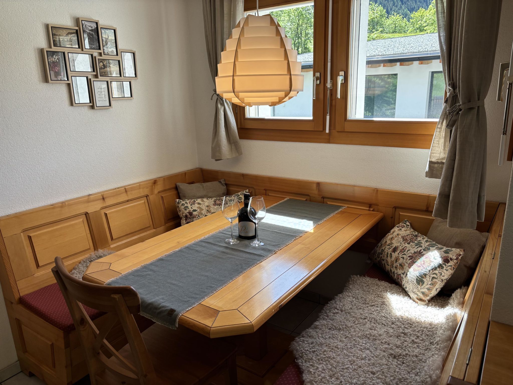 Un coin repas avec une table en bois, des chaises, un banc et une vue sur l’extérieur par une fenêtre.