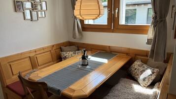 Un coin repas avec une table en bois, des chaises, un banc et une vue sur l’extérieur par une fenêtre.