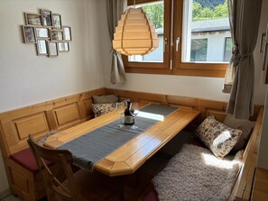 A dining area with a wooden table, chairs, a bench, and a view of the outdoors through a window.