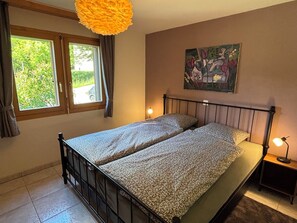 A bedroom with a bed, a window, a painting, and a nightstand.