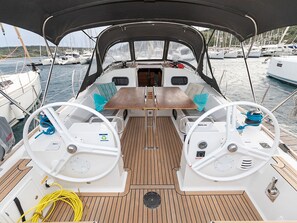 Ein Bootsdeck mit zwei Steuerhörnern, einem zentralen Tisch und einem überdachten Bereich.