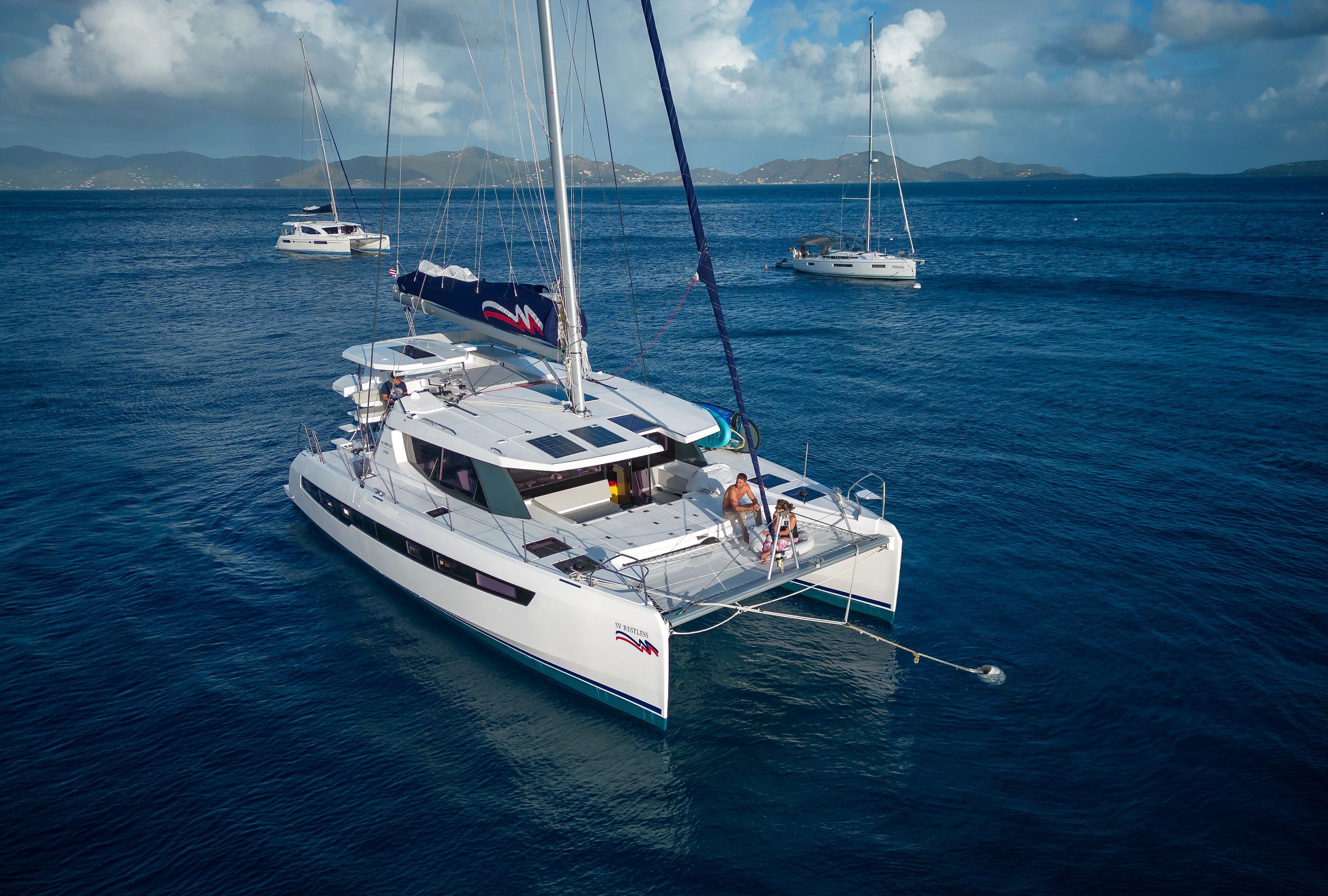 A large yacht with multiple decks and a cabin, sailing in a calm sea with other yachts in the background.