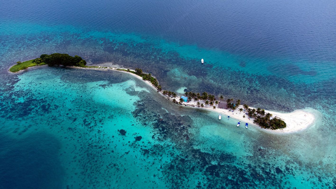 An aerial view of a tropical island with a beach, boats, and clear blue waters.