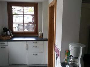 A kitchen with white cabinets, a window with a view of buildings, and a coffee maker on the counter. - ABC Ferienwohnung 3 1. OG Nord-Ost Appartement/Fewo, Dusche oder Bad, WC by Interhome (Fiesch)