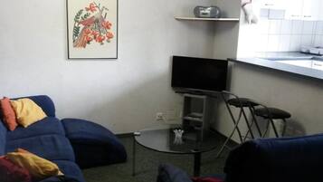 Un espace de vie compact comprenant un canapé, une petite table, un téléviseur et un coin cuisine équipé d’un four à micro-ondes et d’une bouilloire.