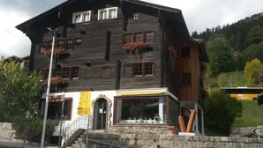 A multi-story wooden building with a stone facade, multiple windows, and a staircase leading to the entrance. - ABC Ferienwohnung 3 1. OG Nord-Ost Appartement/Fewo, Dusche oder Bad, WC by Interhome (Fiesch)