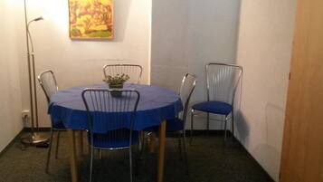 Un petit coin repas avec une table ronde, quatre chaises, une seule plante en pot et un tableau accroché au mur.
