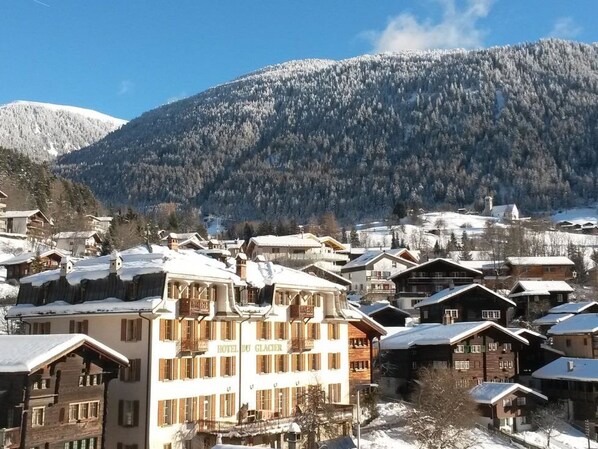 A snow-covered mountain town with wooden buildings and a hotel named 'HOTEL DU GLACIER.'