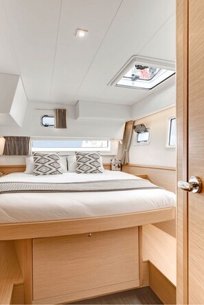 A compact, well-lit bedroom with a skylight, a bed with patterned pillows, and a wooden headboard. - Sun-Kissed Sailing Adventure in the Stunning Islas Cícladas (Paros)