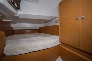 Ein kleiner, abgeschlossener Schlafbereich mit einer Matratze, einem Holzschrank und einem kleinen Regal darüber.