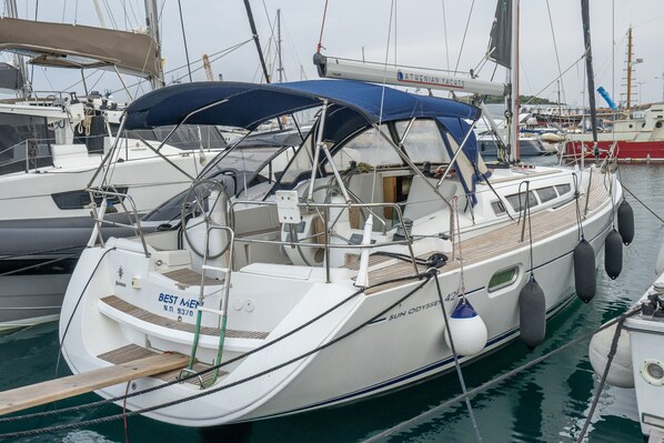 Una barca a vela ormeggiata in una marina, con un ponte coperto, il nome 'SUN ODYSSEY' e una cabina ben visibile.