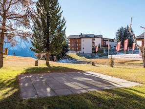 Un bâtiment à étages, une zone pavée au premier plan et une chaîne de montagnes en arrière-plan.