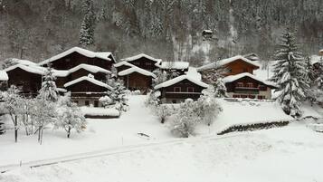 Un village enneigé, avec des maisons en bois, un télésiège et une chaîne de montagnes en arrière-plan.