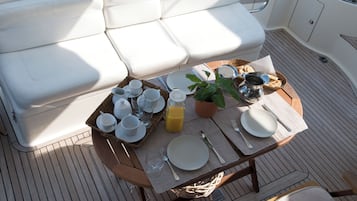 A sunlit outdoor dining area with a table set for breakfast, including plates, cups, and a glass of orange juice.