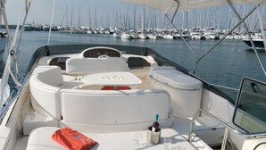 A boat with a white cushioned seating area, a table with a bottle and glasses, and a basket of fruit. - Sun-Kissed Sailing Adventure in Islas Sarónicas (Alimos)