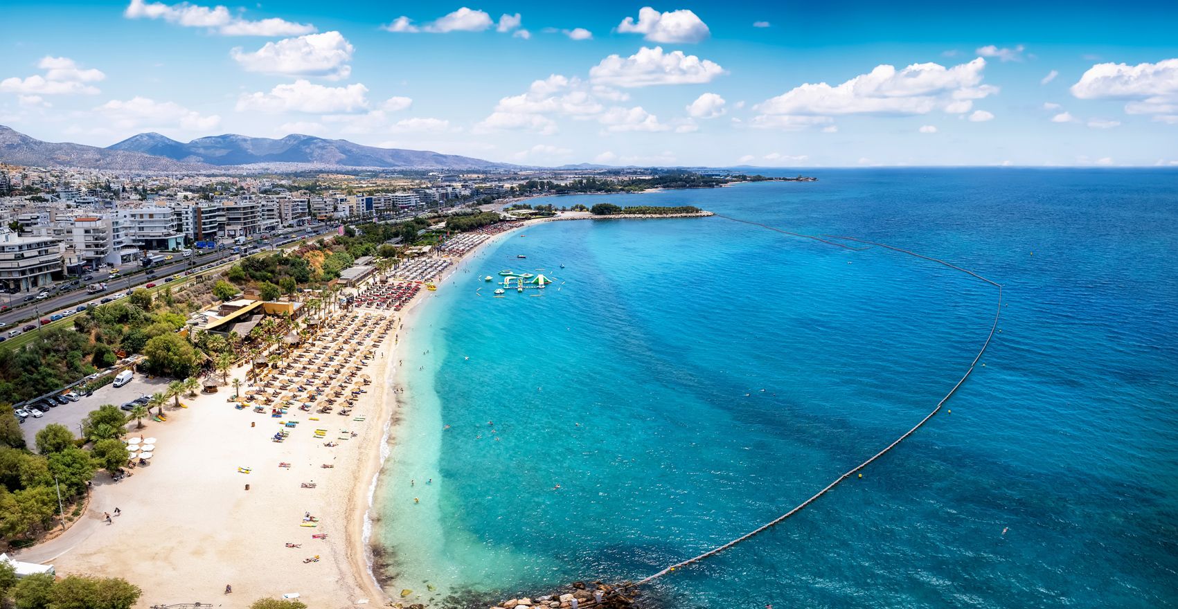 Un paisaje costero con playa, aguas azules cristalinas y una cordillera distante.