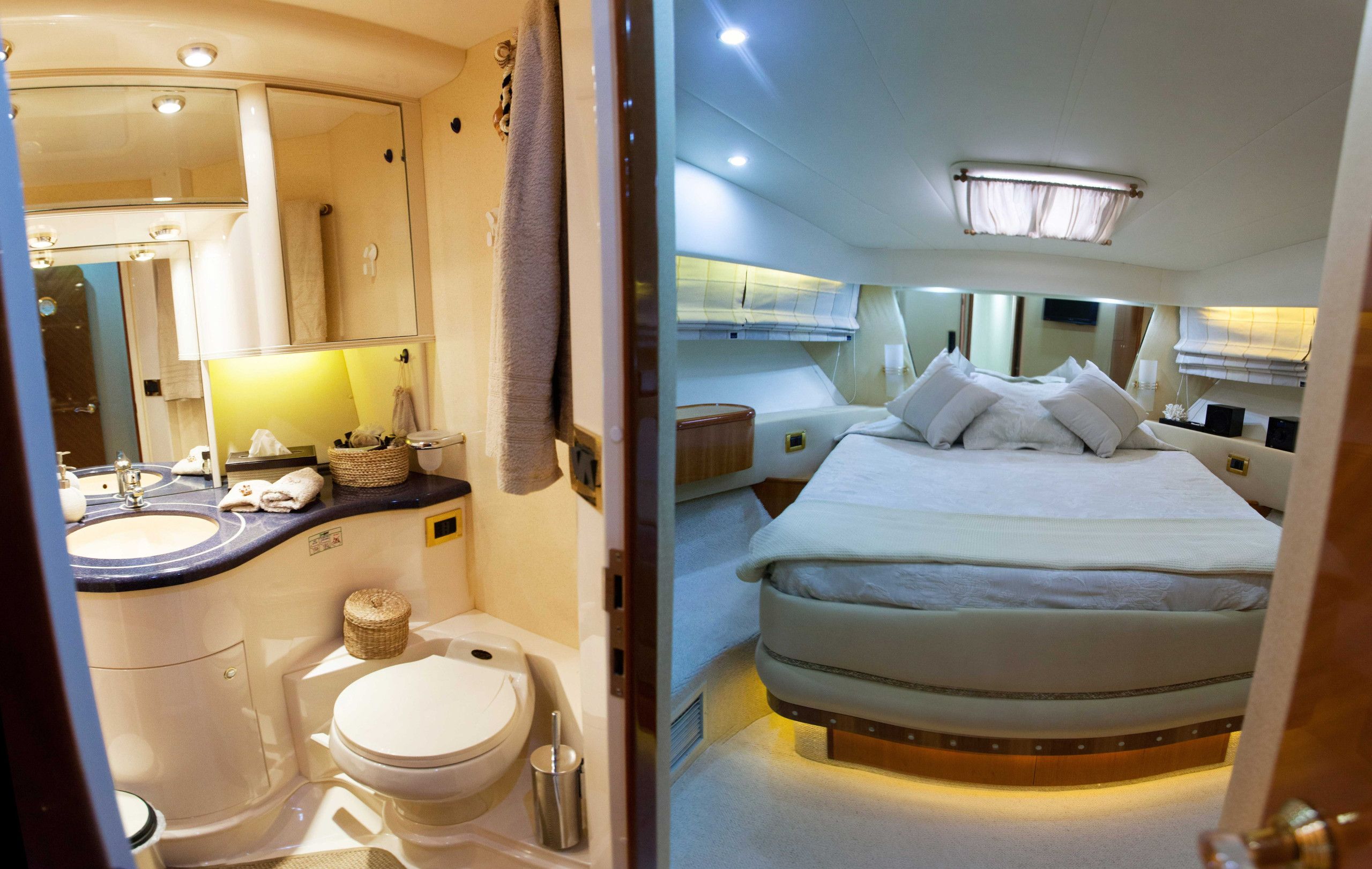Un baño compacto y bien iluminado, con inodoro, lavamanos y espejo. La habitación cuenta con una cama con cabecera, almohadas y una mesita de noche con lámpara.
