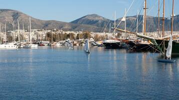 Un puerto deportivo con veleros, un velero con una persona a bordo, y un paisaje urbano con montañas al fondo.