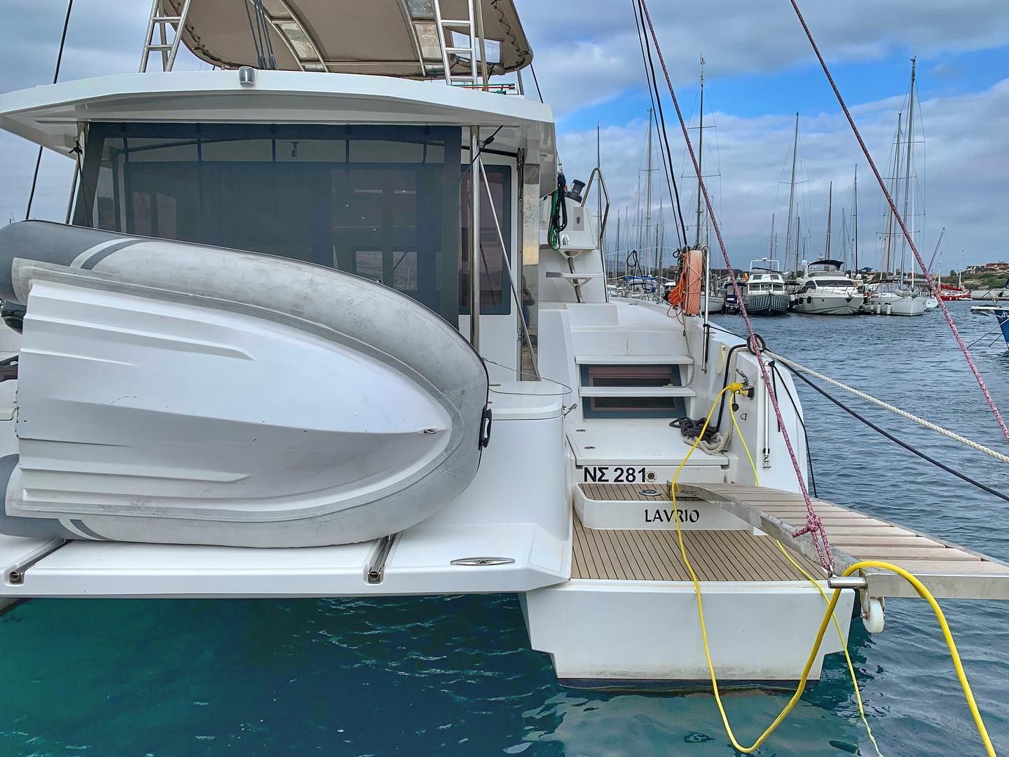 Eine Yacht liegt in einer Marina festgemacht, mit weißem Deck, einem Rettungsring und dem Schriftzug 'LAVRIO' an der Seite.