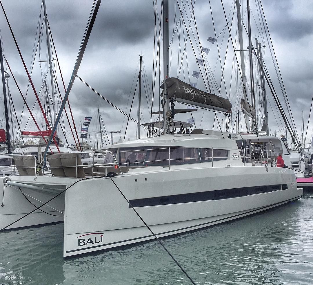 A white yacht named 'BALI' docked at a marina with other boats.