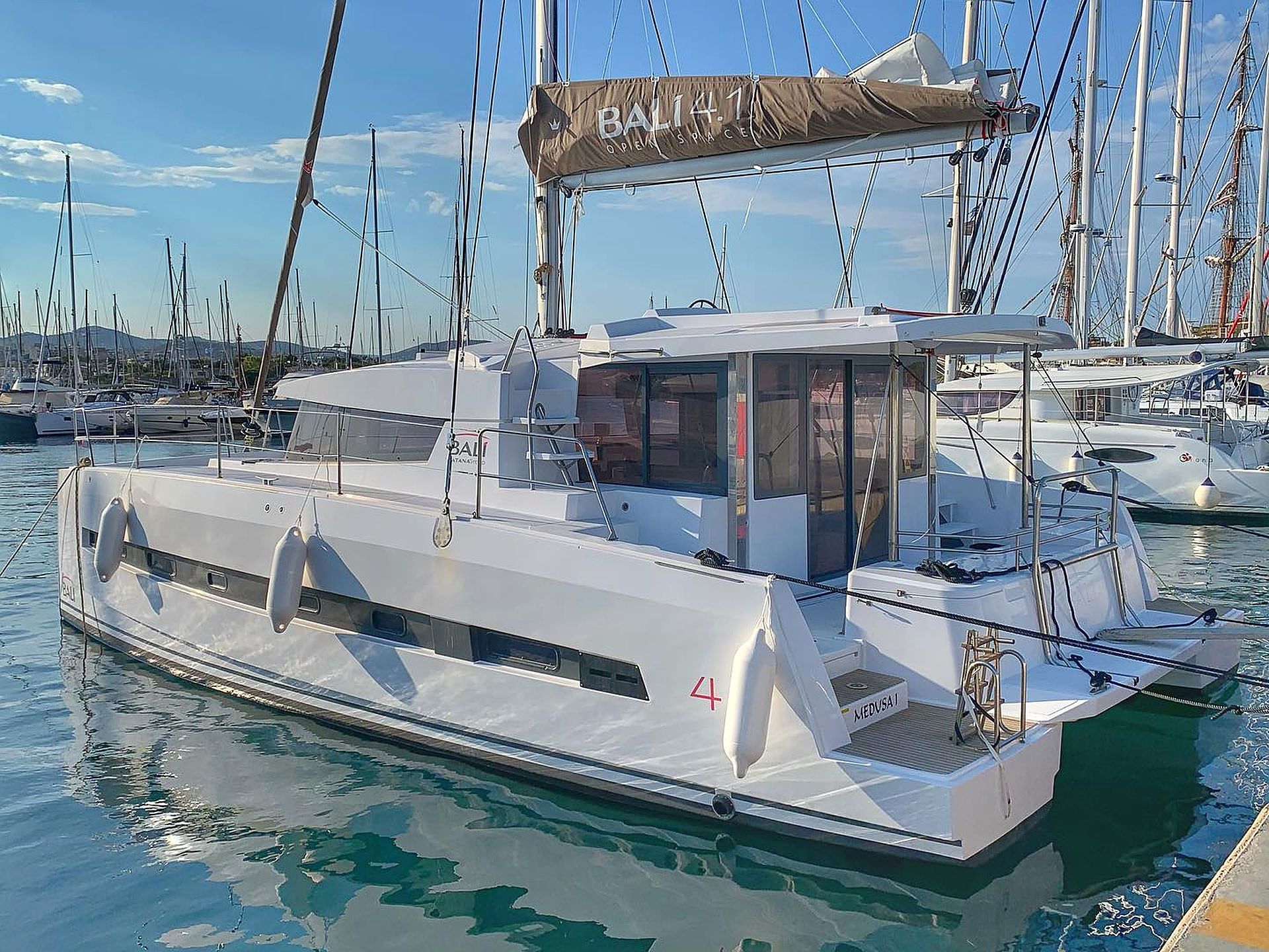 A white motorboat docked at a marina with multiple masts in the background.