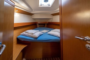 Une petite cabine équipée d’un lit superposé, d’une lucarne et d’une porte en bois.