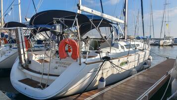 Eine weiße Yacht liegt in einer Marina festgemacht, mit einer überdachten Deckfläche, einer Rettungsboje und dem Namen 'Mesogeios' an der Seite.