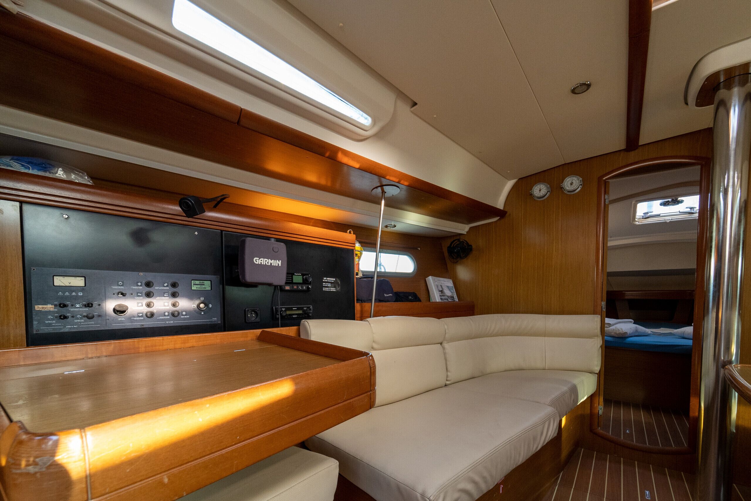 Interior de barco con panel de control, zona de estar acolchada y un pequeño espacio dormitorio cerrado.