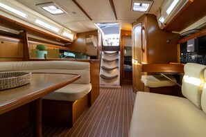 A boat interior with a dining area, seating, a kitchen, and a control panel.