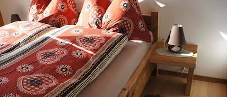 Een bed met een geborduurd sprei en meerdere kussens, een bedlampje en een houten nachtkastje.