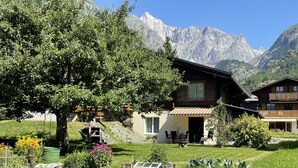 Un albergue de montaña con jardín, mesas al aire libre y vistas a las montañas.