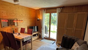 Un ambiente acogedor con detalles de madera, una mesa de comedor con sillas, un sofá, un televisor y un ventanal corredizo que da a un espacio exterior.
