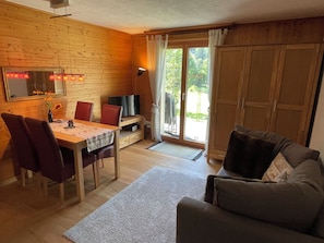 Ein gemütliches Zimmer mit Holzvertäfelung, einem Esstisch mit Stühlen, einer Couch, einem Fernseher und einer Glastür zum Außenbereich.