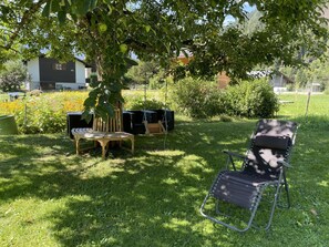 A garden with a wooden bench, a metal chair, and a tree with green apples. - Sweda EG Süd Appartement/Fewo, Dusche oder Bad, WC 2 Zimmerwohnung, 2-Betten by Interhome (Fiesch)