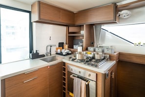A compact kitchen with wooden cabinets, a stainless steel stove, and a window providing natural light. - Sun-Kissed Sailing Adventure in the Ionian Islands (Paleros)