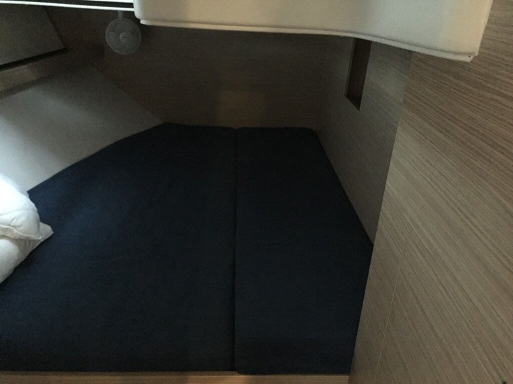 A bed with a dark mattress and a white pillow in a room with a wooden floor and a white wall.