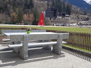 A stone bench with a potted plant, a red flag, and a view of a town with buildings and mountains in the background. - Lischa 3. OG Süd Appartement/Fewo, Dusche oder Bad, WC by Interhome (Fiesch)